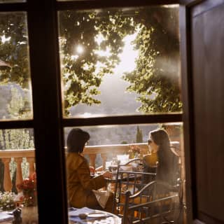 View from inside Miró restaurant to the terrace where two women sit in golden light at a table, enjoying incredible views.