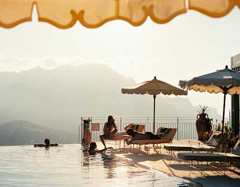 Two friends relax in the pool and chat to three more who sit on loungers enjoying the views and perks of the La Piscina club.